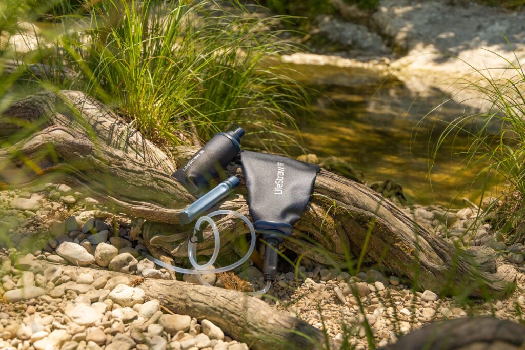 A Lifestraw Peak Series Gravity and straw filter on a log by a stream.