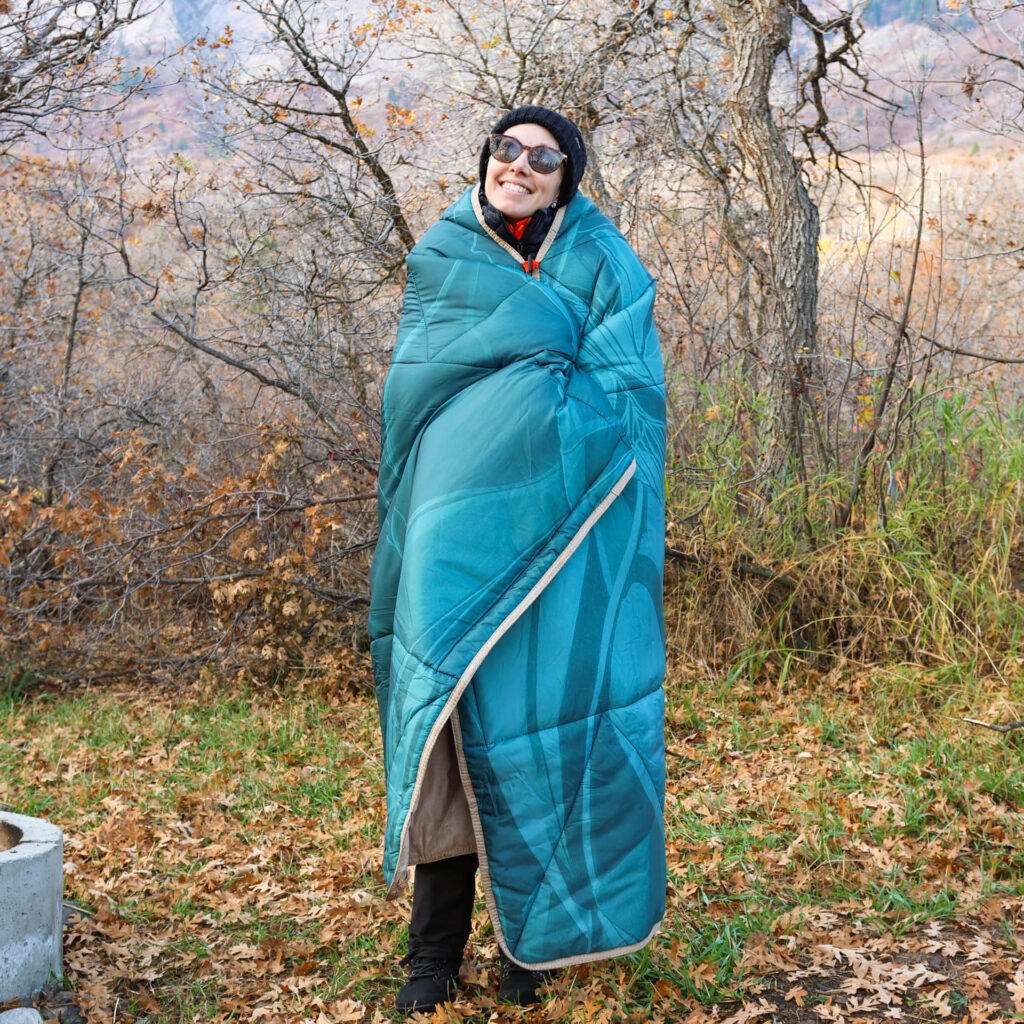 A woman is wrapped up in an Ignik Topside Heated camp blanket.