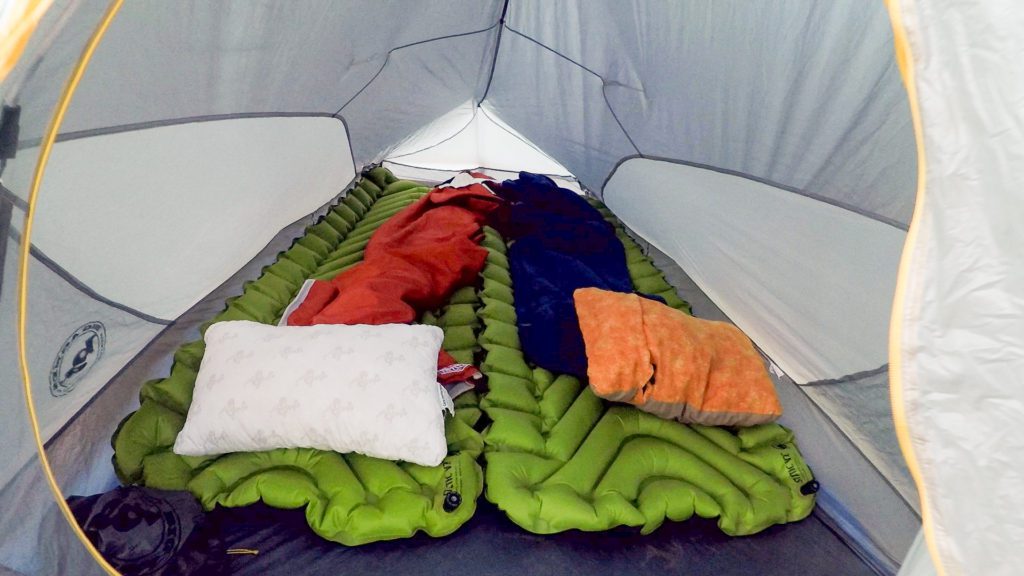The inside of a tent with sleeping pads, sleeping bags and pillows.