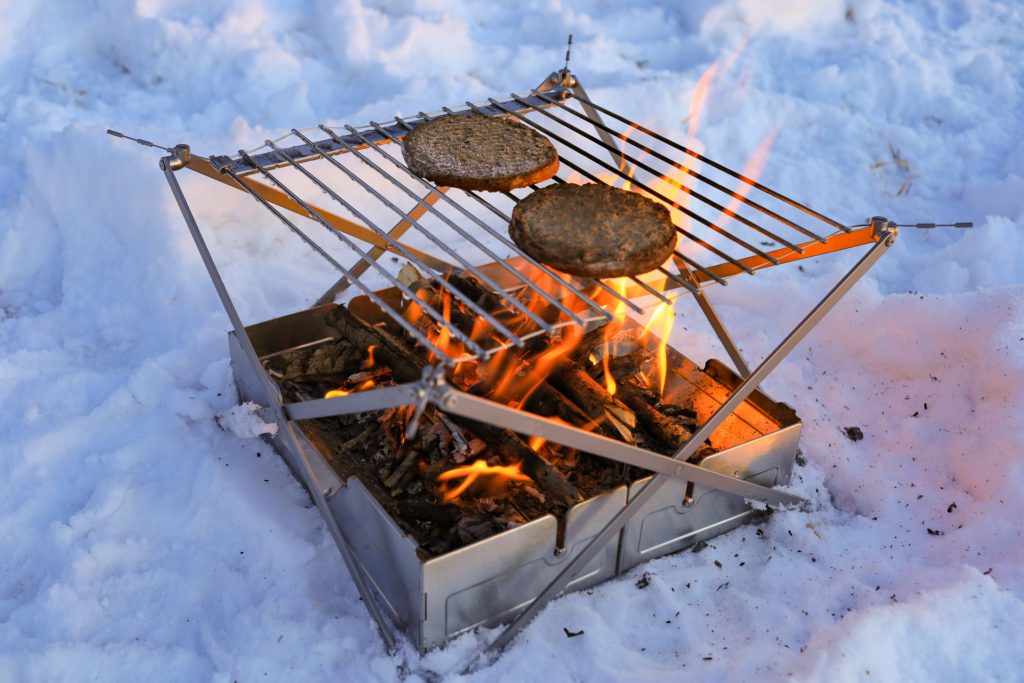 Burgers cooking on the Wolf and Grizzly Fire Safe and Grill portable fire pit.