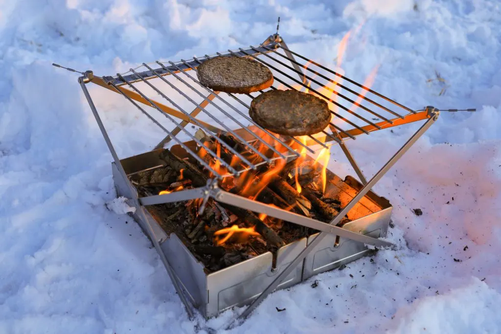 Burgers cooking on the Wolf and Grizzly Fire Safe and Grill portable fire pit.