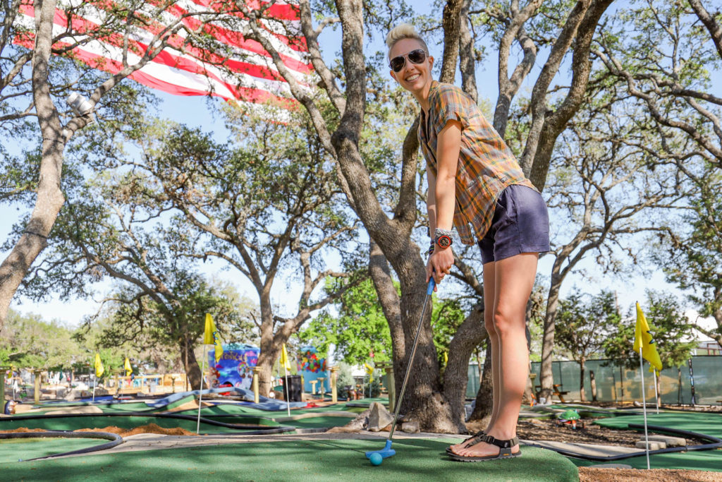 memorial day sales on outdoor gear: playing mini golf in front of a large American Flag