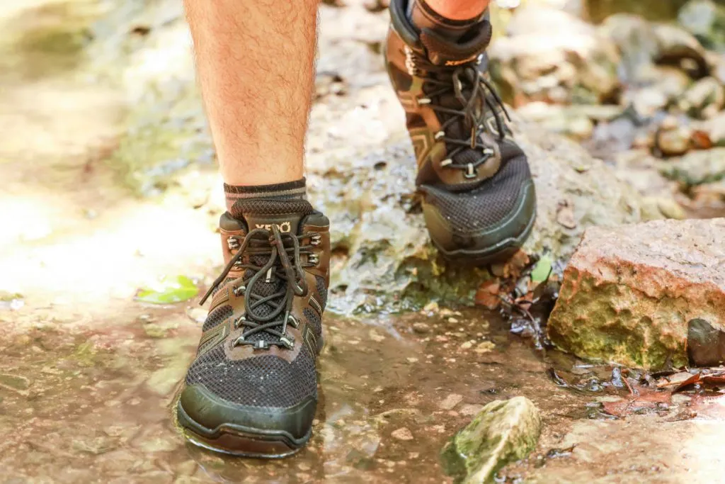Xero Shoes Xcursion Fusion Barefoot hiking boot in brown, crossing a creek.