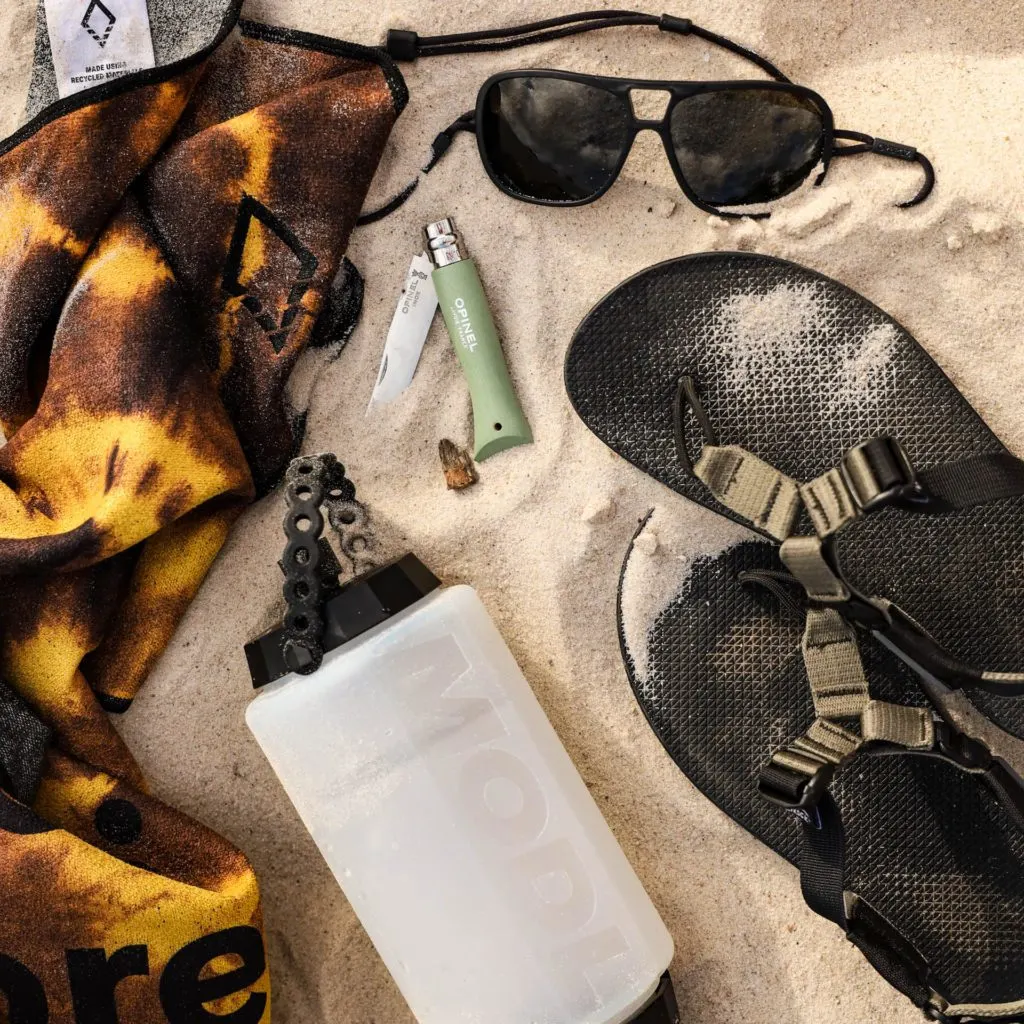 gear for beach camping: sandals, water bottle, pocket knife, sunglasses, towel.
