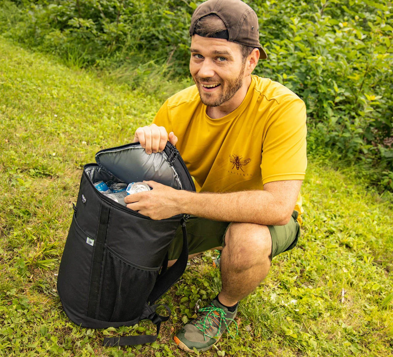 A smiling man grabs a can out of a backpack cooler filled with ice.