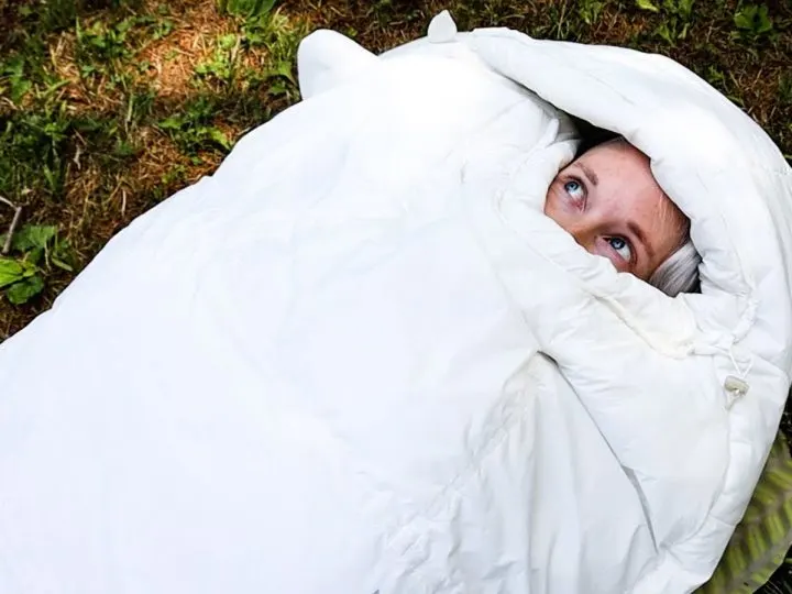 Just a woman's face peering out of a white sleeping bag.