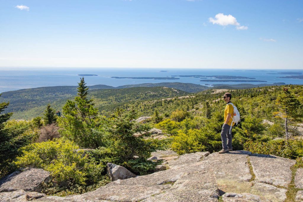 A man looks out over the mountains toward the ocean from the top of Cadillac Summit in Acadia National Park.