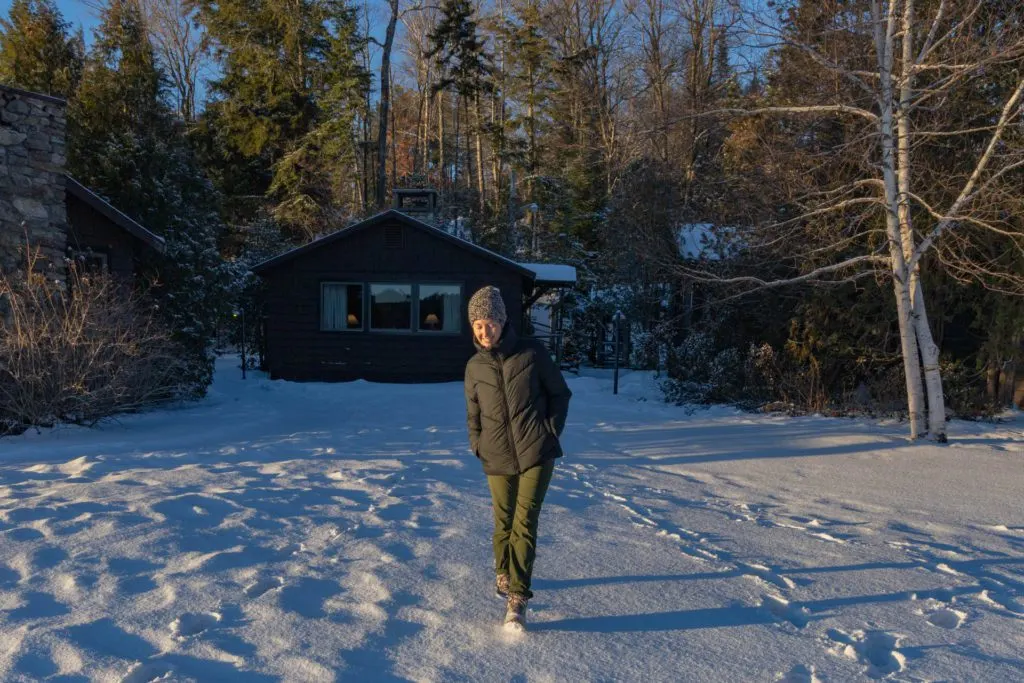 Woman in a Save the Duck recycled coat in front of a cabin in the snow.