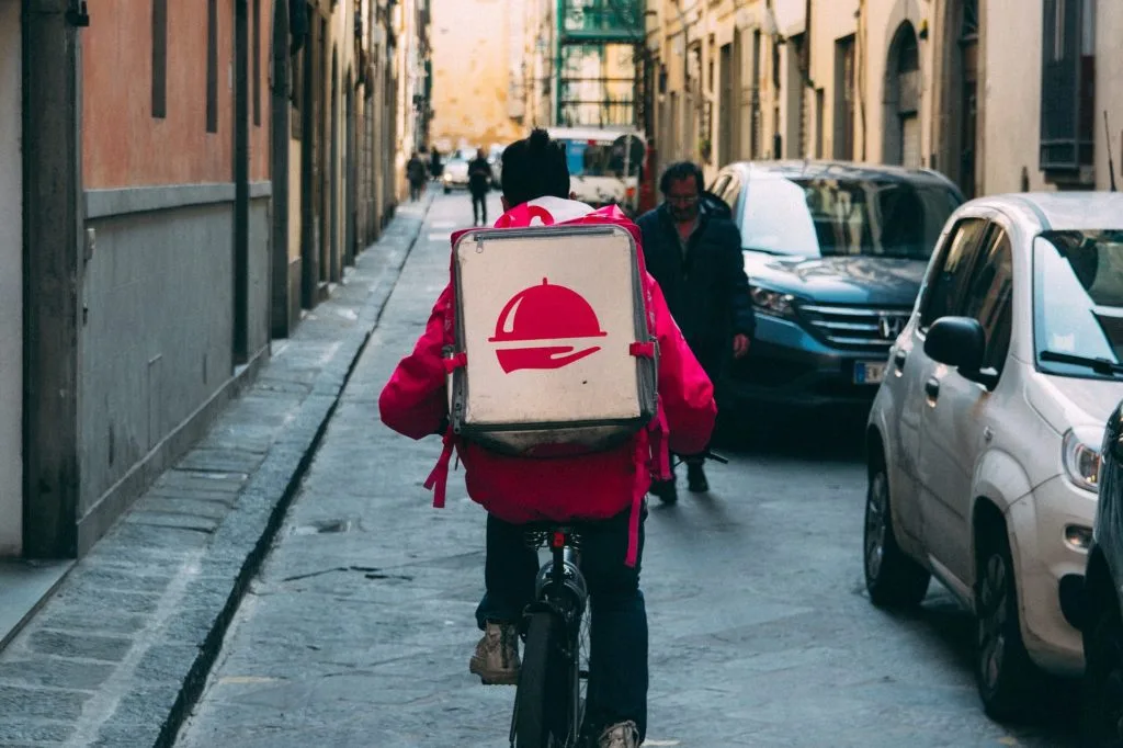 A delivery person carries a backpack on a bike.