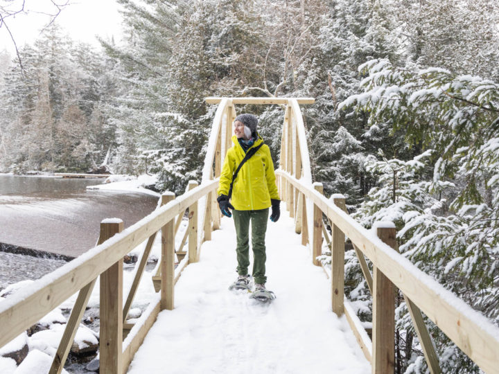 woman walking over a footbridge in the snow with snowshoes.