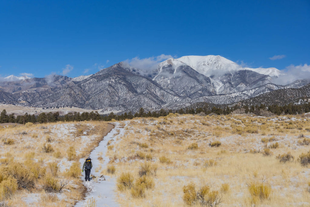 Hiker on a snowy trail headed toward mountains in Great Sand Dunes National Park.
