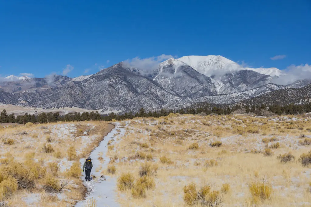 Man hiking with the Deuter Futura Air Trek Backpack in Great Sand Dunes National Park with mountains in the background.