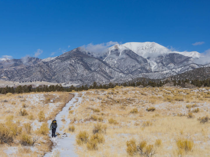 Hiker on a snowy trail headed toward mountains in Great Sand Dunes National Park.