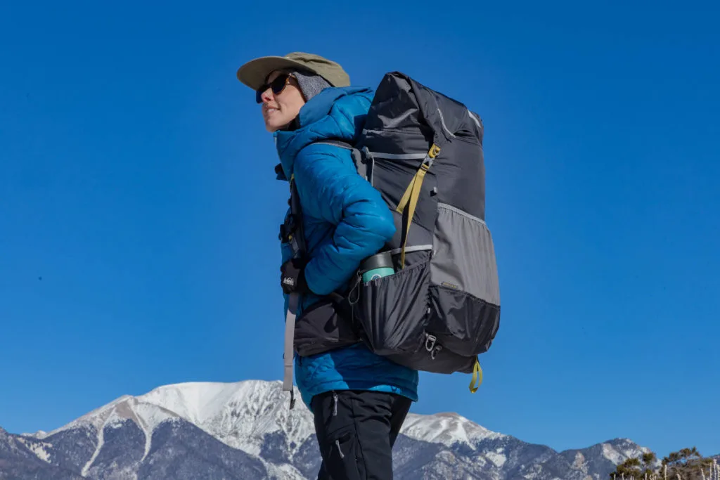 A woman with backpack in front of snowy mountain.