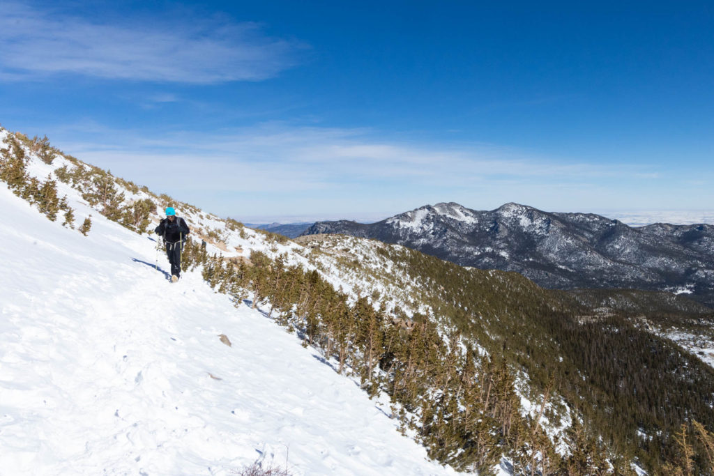 Man hiking on a snowy ridge with a backdrop of mountains.