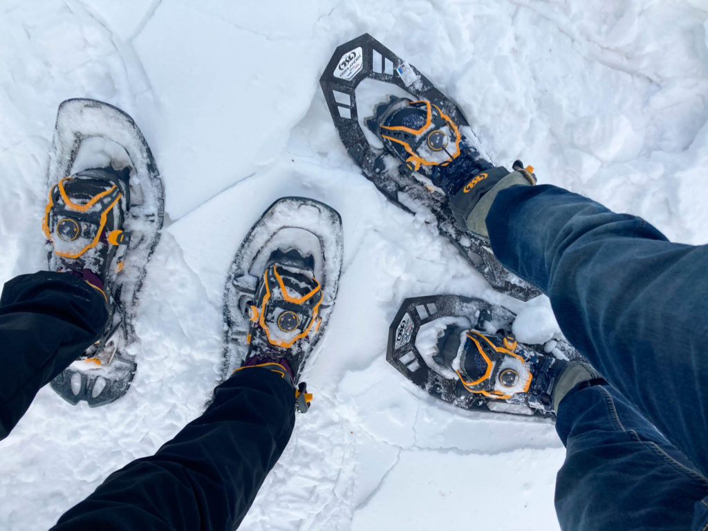 Two pairs of feet in TSL snowshoes in the snow.