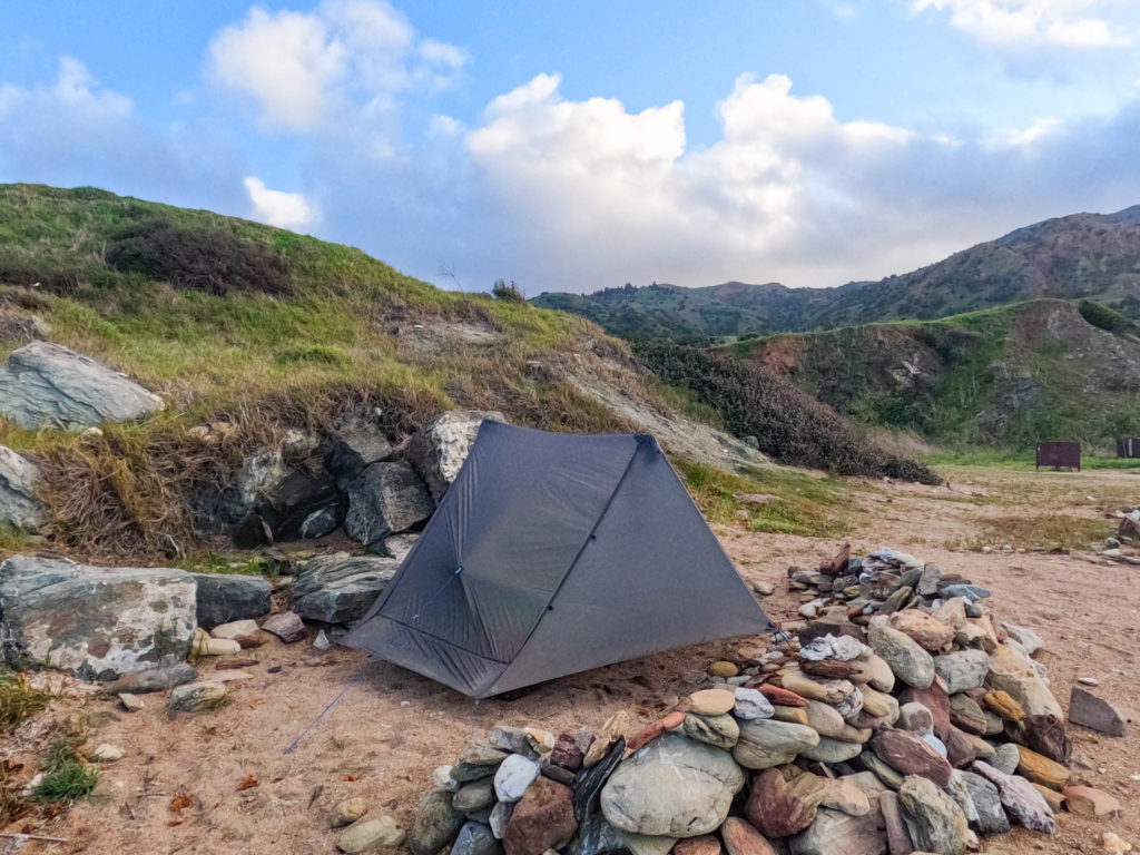 The Gossamer Gear The One ultralight tent pitched on the beach with mountains in the background.