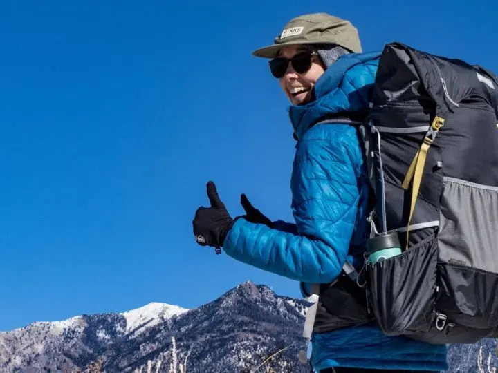 Gifts for backpackers: a woman with an ultralight backpack gives a thumbs up in front of mountains.