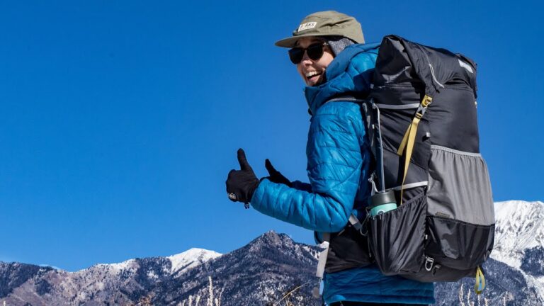 Gifts for backpackers: a woman with an ultralight backpack gives a thumbs up in front of mountains.