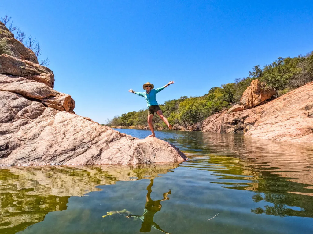 A woman with her hands joyfully in the air on rocks by the water at Inks Lake State Park in Burnet County.