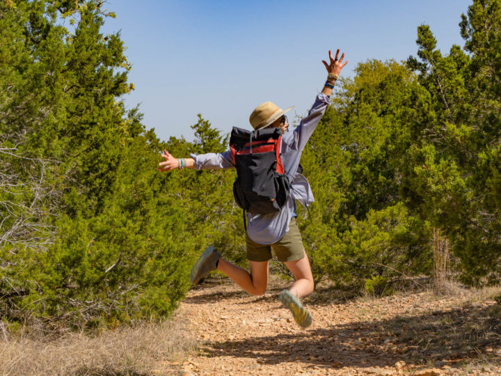 A woman jumps for joy wearing a Waymark Gear Co.MILE 28 backpack.