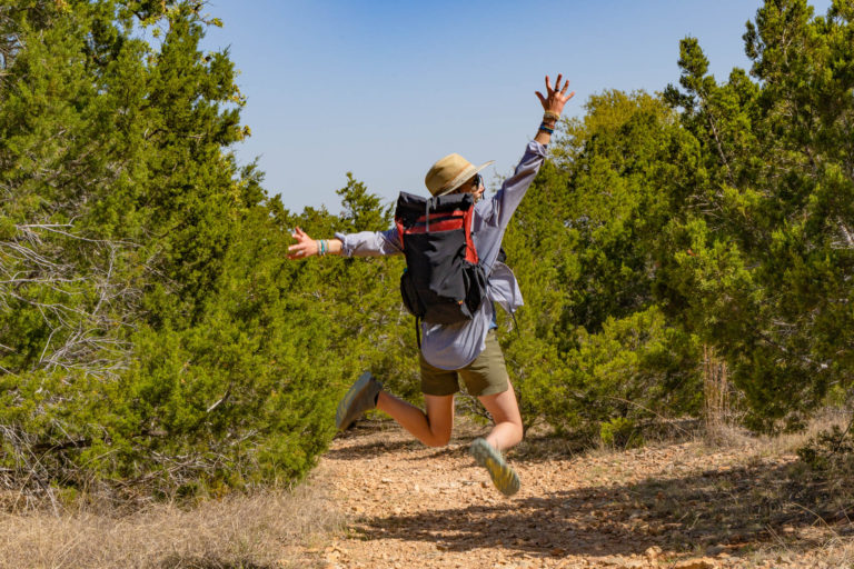 A woman jumps for joy wearing a Waymark Gear Co.MILE 28 backpack.