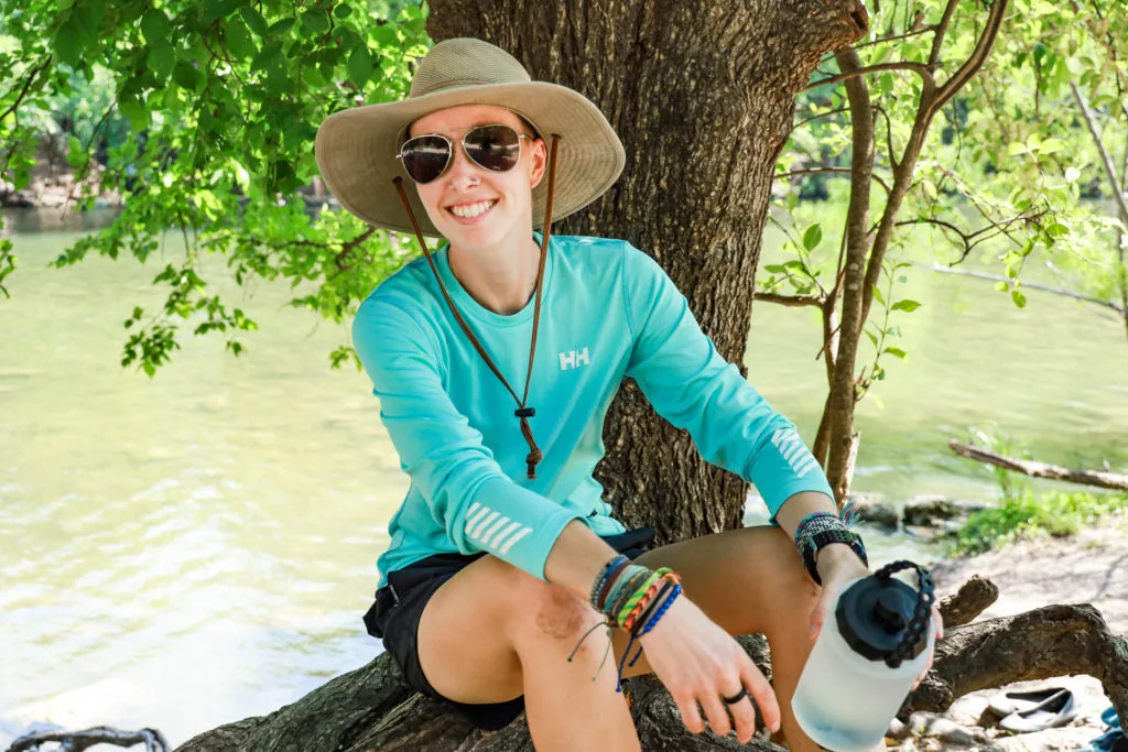 Woman sitting by a swimming hole wearing a Helly Hansen long sleeve shirt.