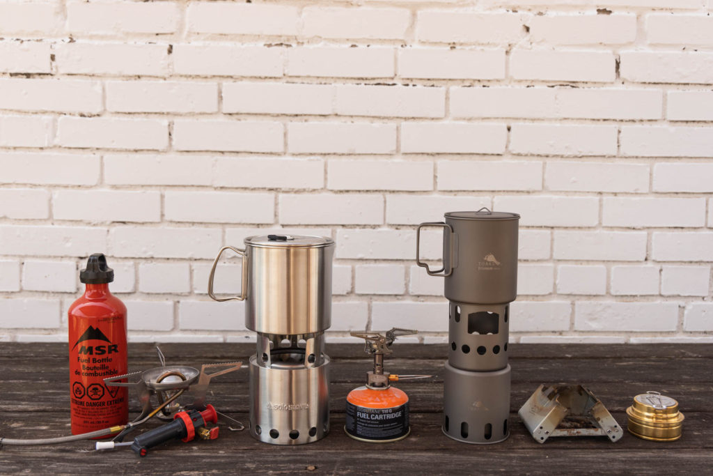 Backpacking stoves lined up: Liquid fuel, Solo Stove, canister Stove, wood-burning stove, solid fuel stove, and alcohol stove.