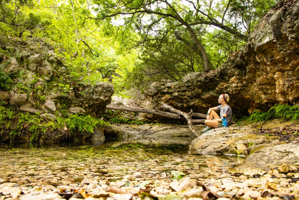 woman sitting on a rock by a spring.