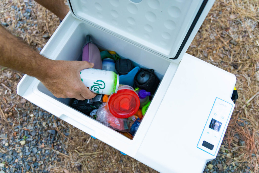 A hand pulling a can of water out of the interior of the GoSun Chill electric cooler.