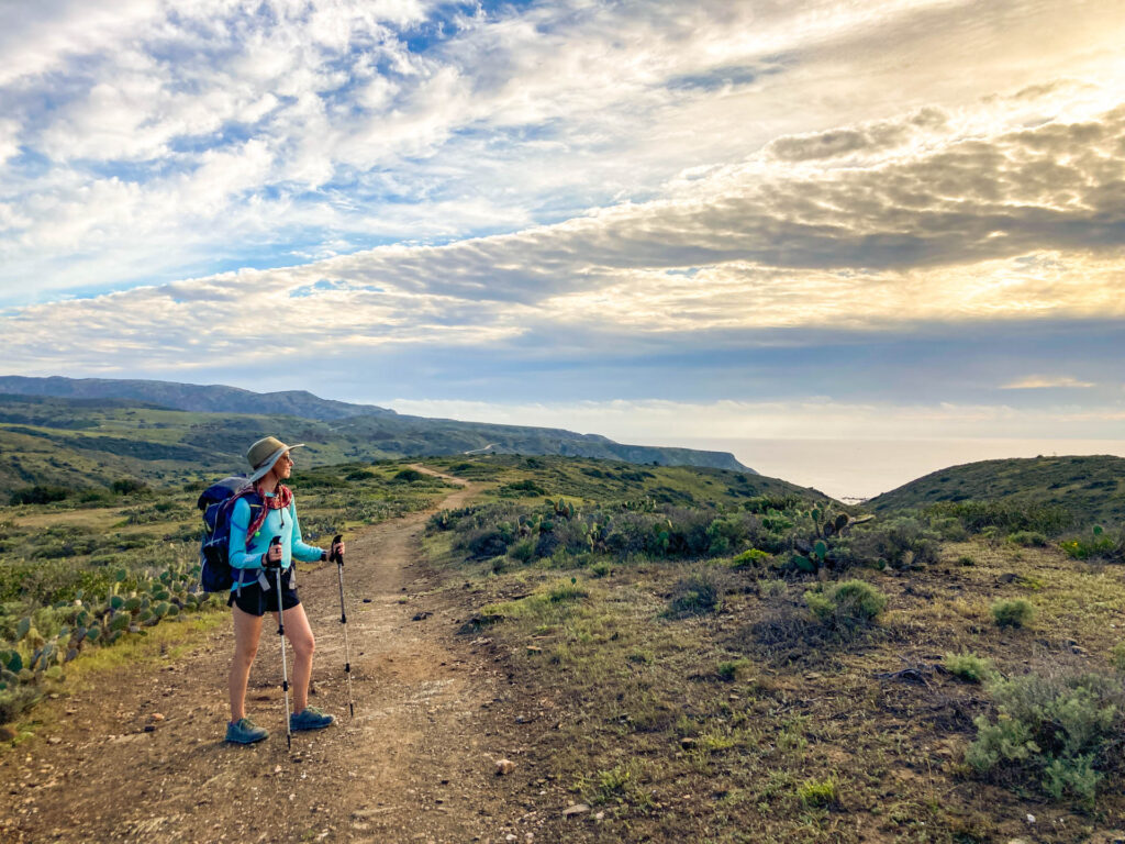A woman in backpacking gear looks out over the landscape and the ocean on Catalina Island, California.