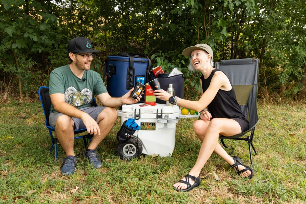 A couple cheerily clinks glasses outdoors while enjoying camp cocktails.