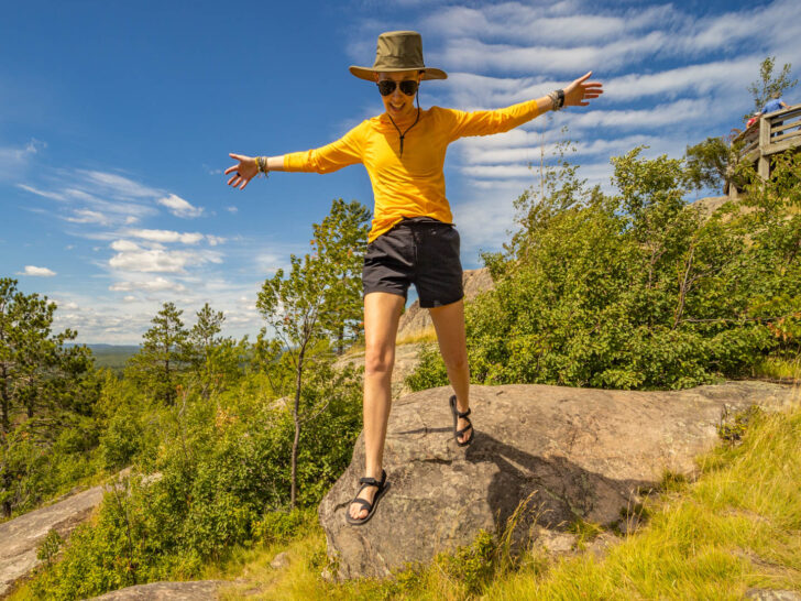 a woman jumps off a rock in hiking sandals.