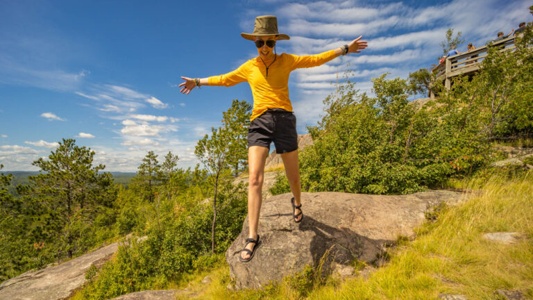 a woman jumps off a rock in hiking sandals.