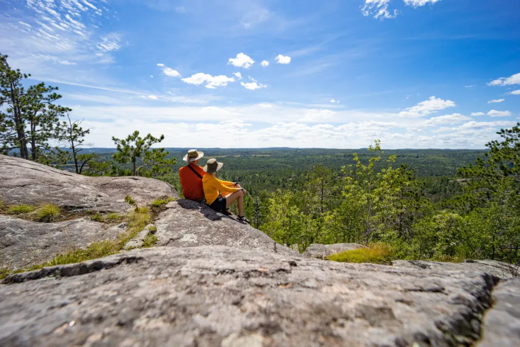 Two people sit on a cliff and look out over the forest.