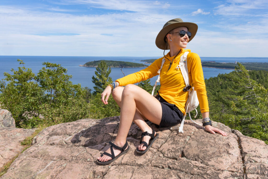 A woman sits on a rock on a mountain in front of Lake Superior wearing the Outdoor Research Echo Hoody in Marquette, Michigan.