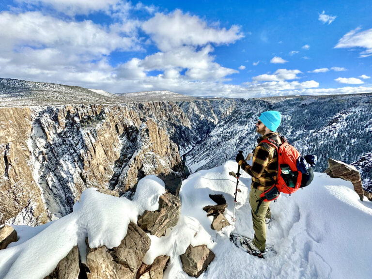 A man snowshoeing and enjoying the view of the snowy canyon at Black Canyon of the Gunninson National Park in Colorado.