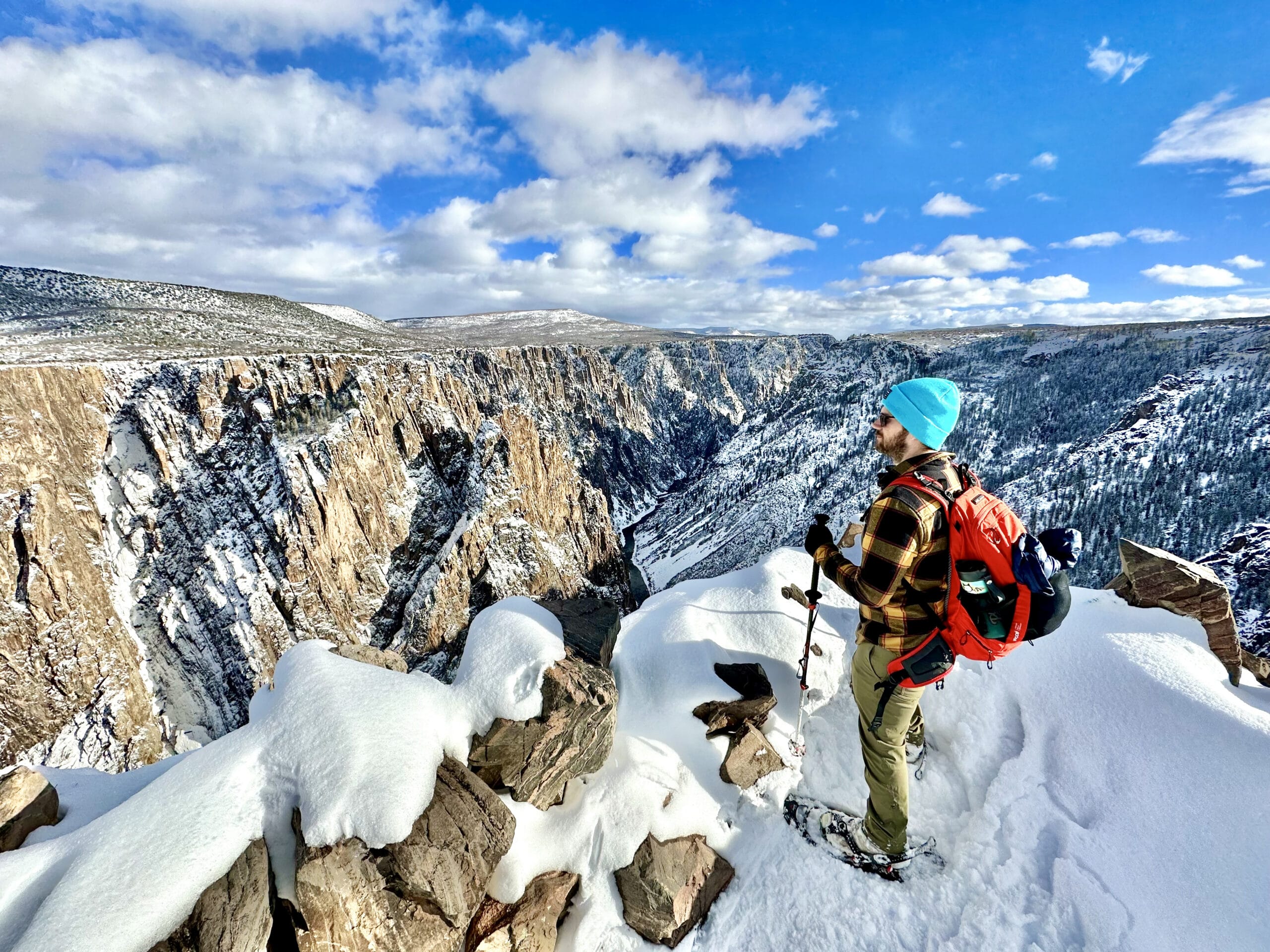A man snowshoeing and enjoying the view of the snowy canyon at Black Canyon of the Gunninson National Park in Colorado.