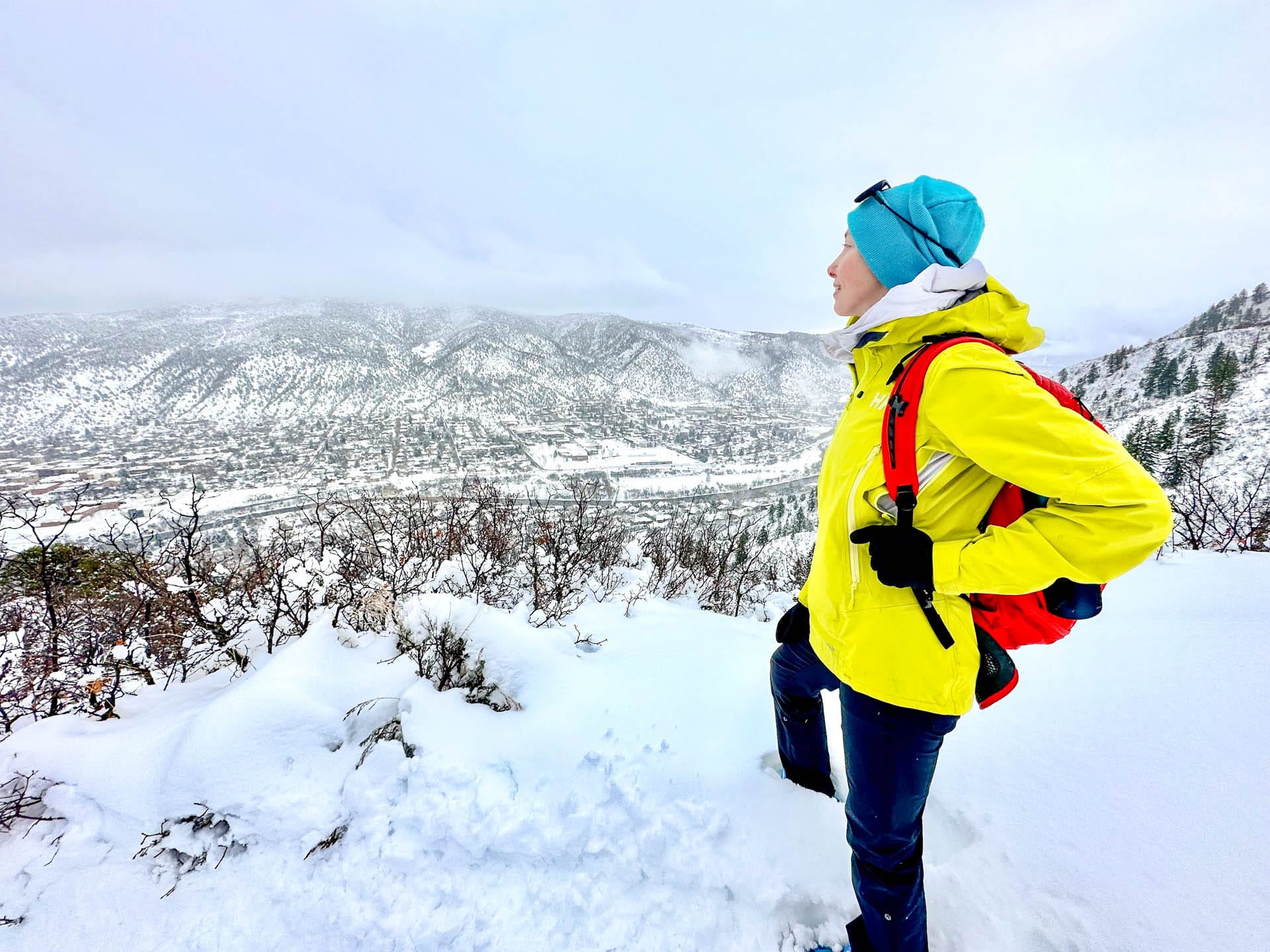 A woman stands on a snow-covered cliff looking at mountains.