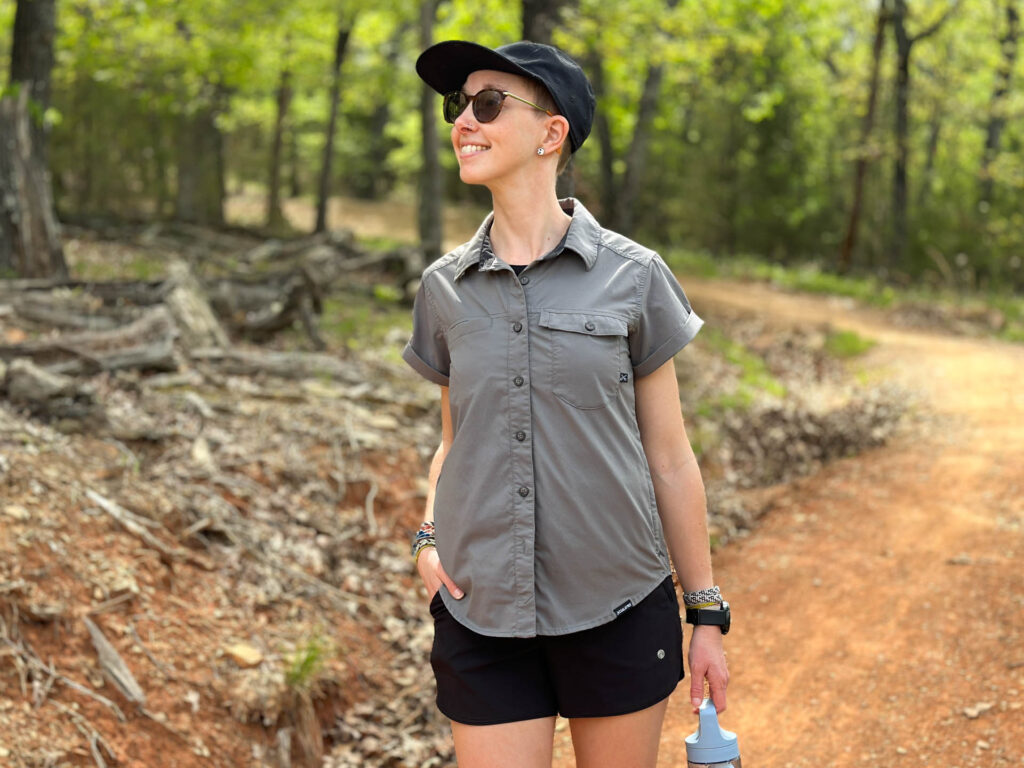 A woman walks a trail smiling in a Coalatree Switchback shirt.