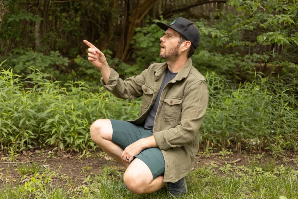 A man squats in a silly pose wearing an Outerknown Chroma Blanket Shirt in olive green.