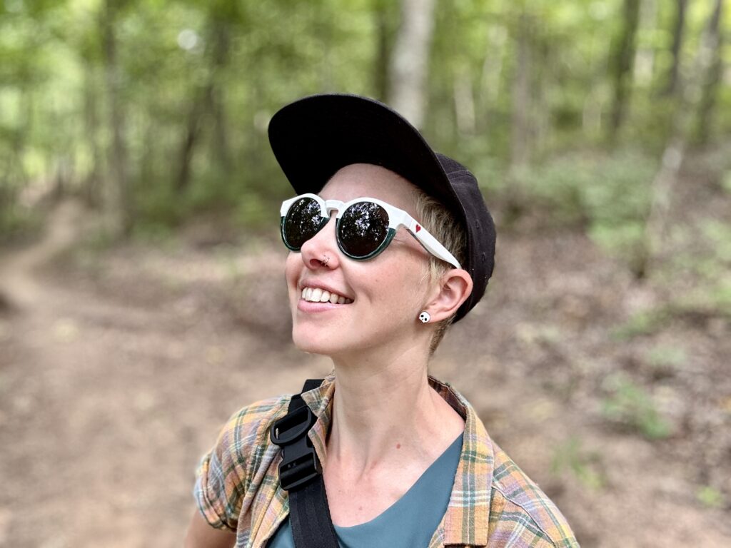 a woman looks up and smiles in the woods. She is wearing stylish Zeal sunglasses.