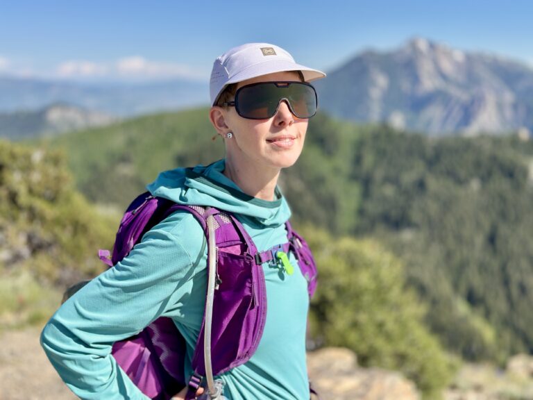 A woman wears sunglasses and a hat on a peak.
