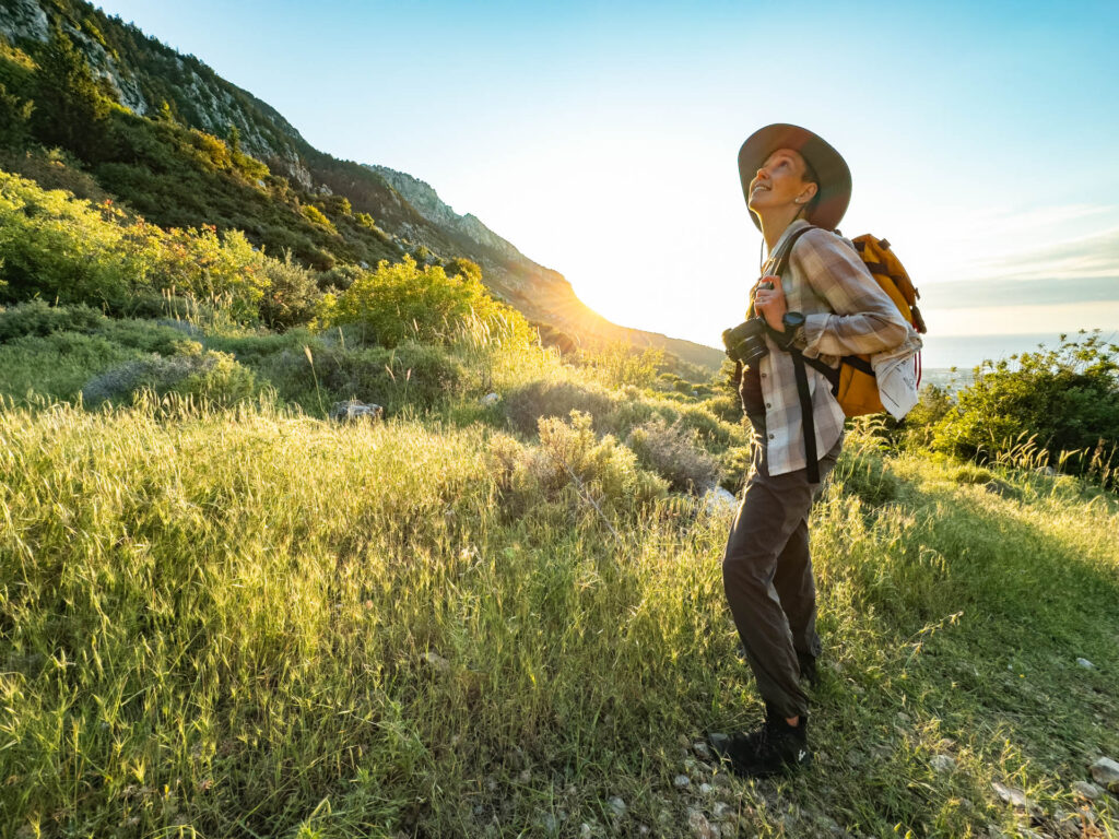 a woman with a backpack looks up into the mountains near sunset.