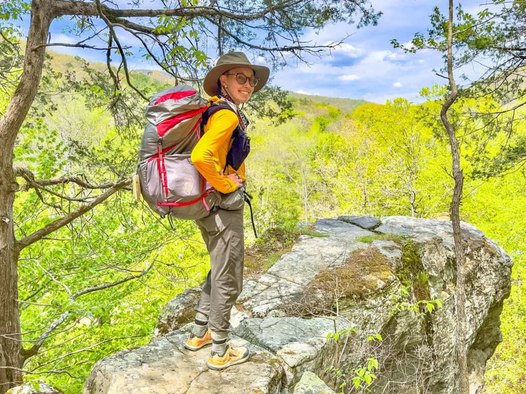 A woman wearing the Osprey Eja Pro 55L backpack smiles on a cliff.