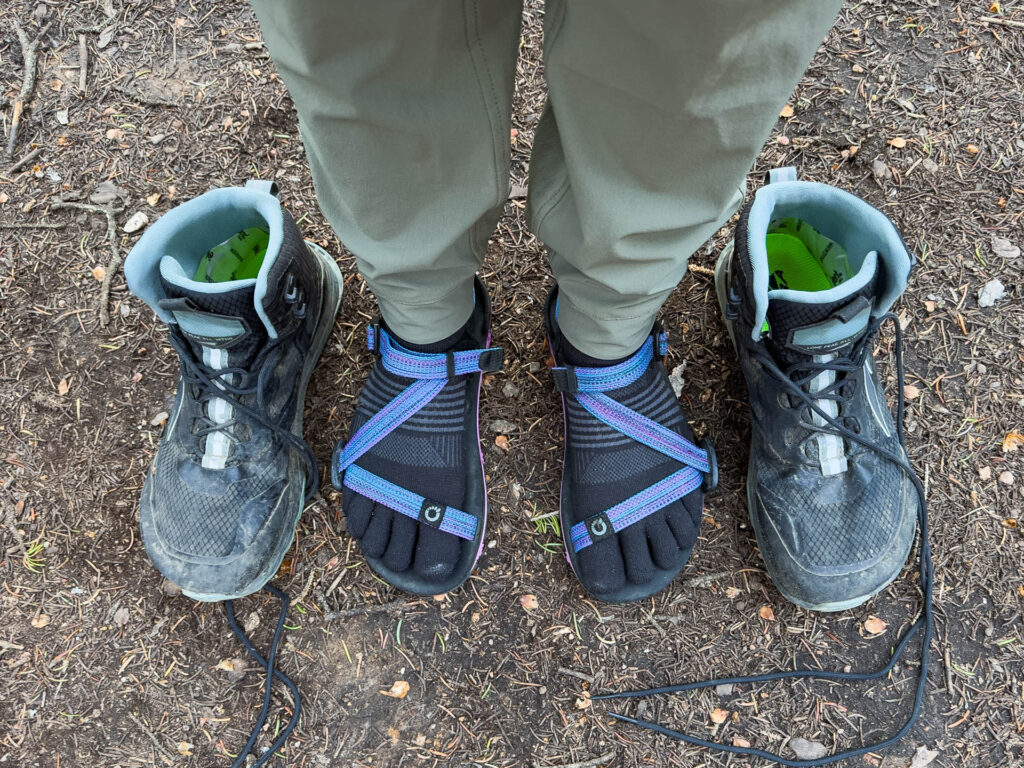 A pair of feet in toe socks and sandals in between hiking boots.