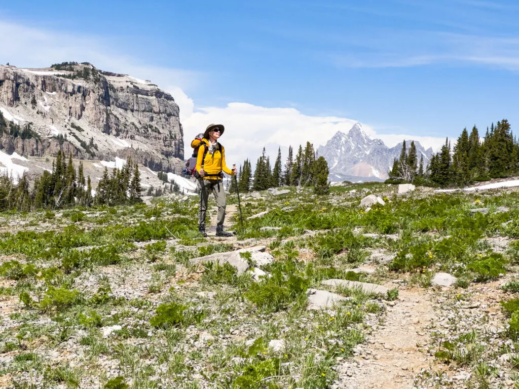 A woman with a backpack stands in front of mountains.