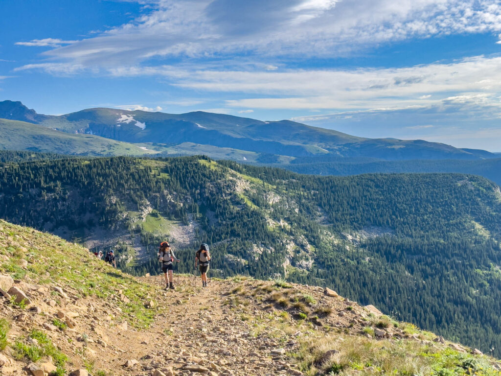Backpacking in Colorado during The Fjallraven Classic USA: two hikers trek up a trail with mountains in the background.