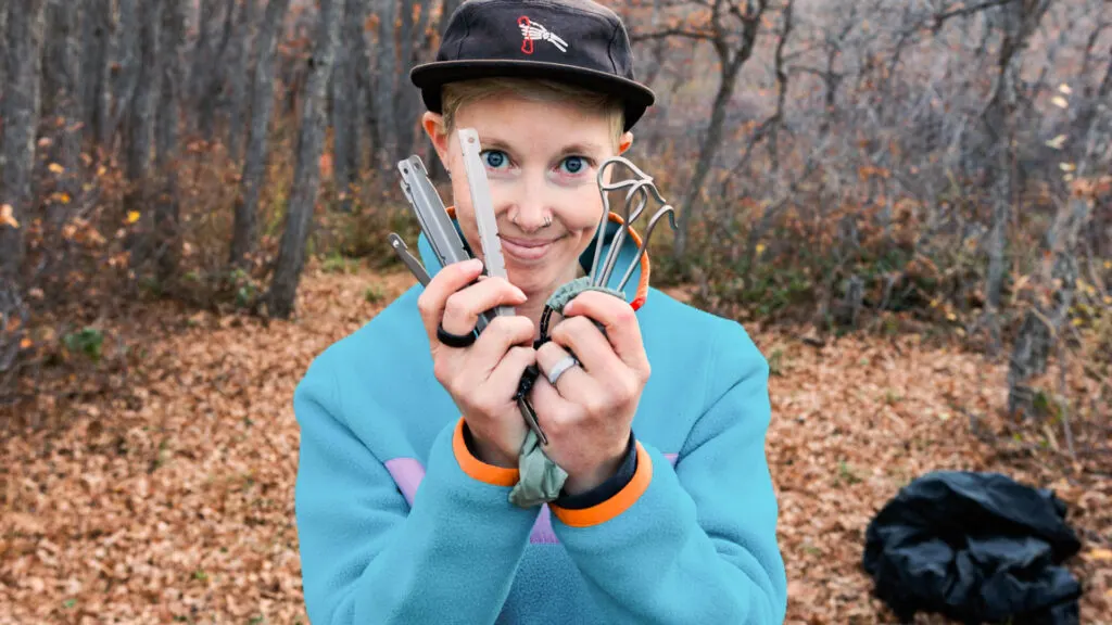 A woman holds up tent stakes and smiles.