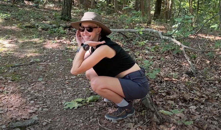 A woman squats in the woods with her Gnara Go There Shorts on.